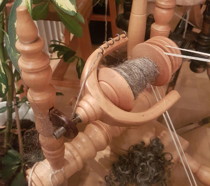 Närbild av en gammaldags spinnrock i trä med ulltråd på spolen.