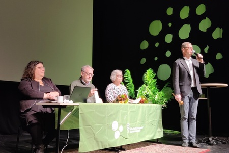 Fyra personer deltar i ett panelsamtal på scen, en står och talar i mikrofon.