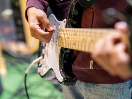 Närbild av en person som spelar elgitarr, fokus på händer och gitarrens hals.