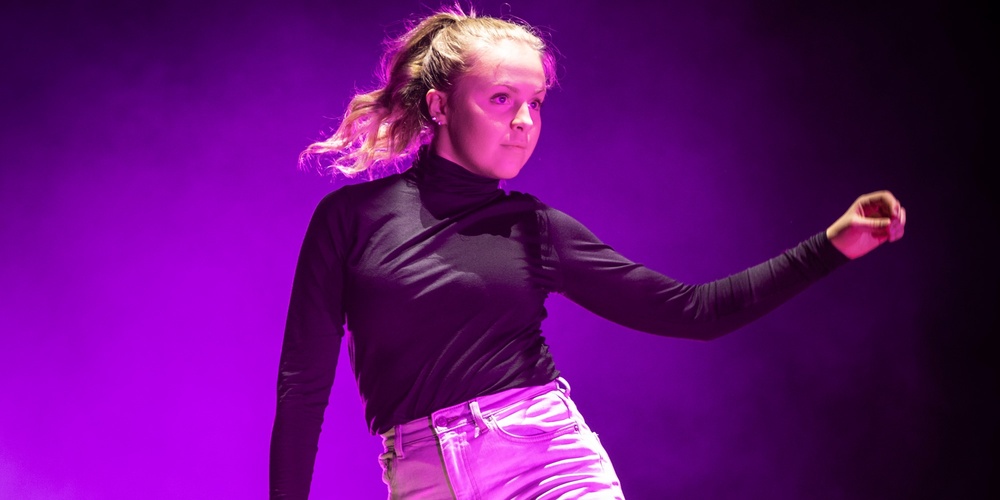 En person dansar barfota på en scen med lila ljus och rökeffekter.