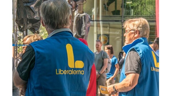 Två personer som har västar som det står Liberalerna på ryggen står på en gata med folk.