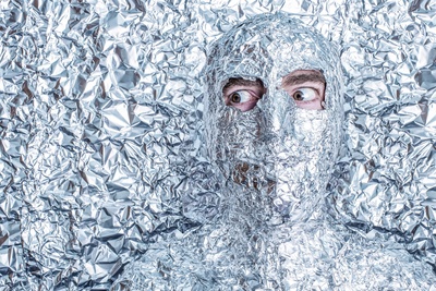 En person är täckt av skrynklig aluminiumfolie mot en bakgrund av mer aluminiumfolie.