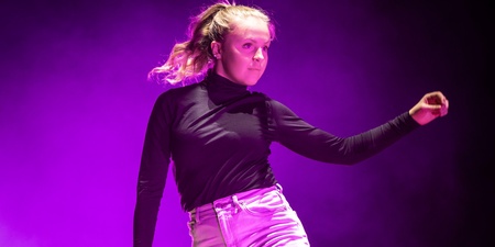 En person dansar barfota på en scen med lila ljus och rökeffekter.