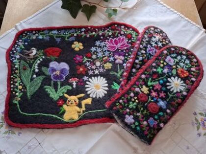 Broderad duk och vantar med färgglada blommor och Pikachu-motiv på en vit duk.