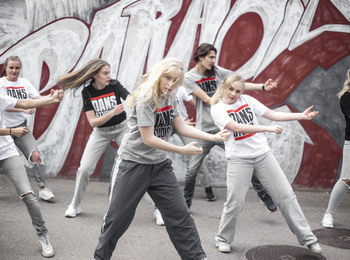 En grupp unga personer dansar hiphop utomhus framför en graffitivägg.