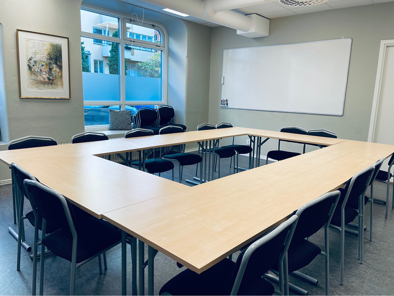 Ett tomt konferensrum med U-formad borduppställning, svarta stolar, whiteboard och stort fönster.