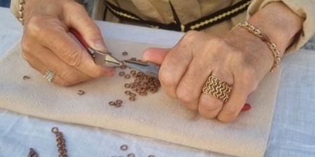 En person arbetar med smyckestillverkning och använder tänger för att böja små metallringar på en duk.