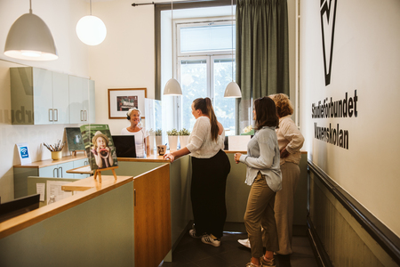 Fyra personer samtalar vid en reception i en ljus och modern kontorsmiljö med stora fönster.