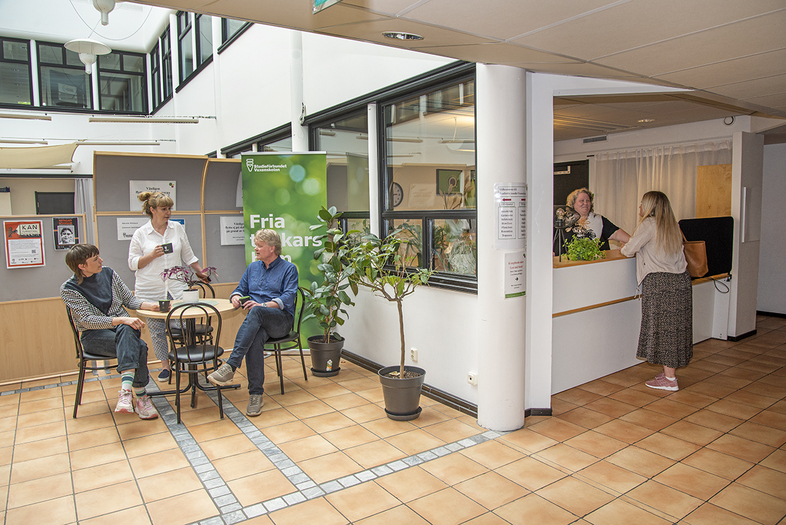 Väntrum på vårdcentral med sittande och stående personer samt reception.