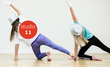 Två personer dansar i studio, bär hattar och handskar, sträcker armarna uppåt mot väggen.