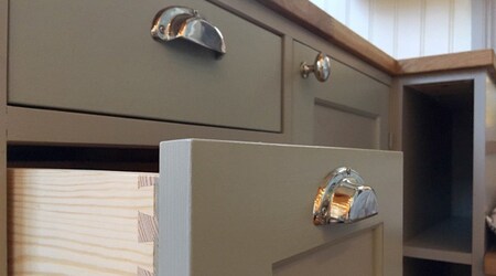 Närbild på gröna kökslådor och skåp med silverfärgade handtag, en låda är utdragen.