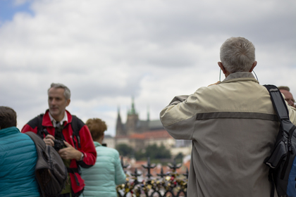 Flera personer står utomhus, några fotograferar, med en stadssilhuett och slott i bakgrunden.