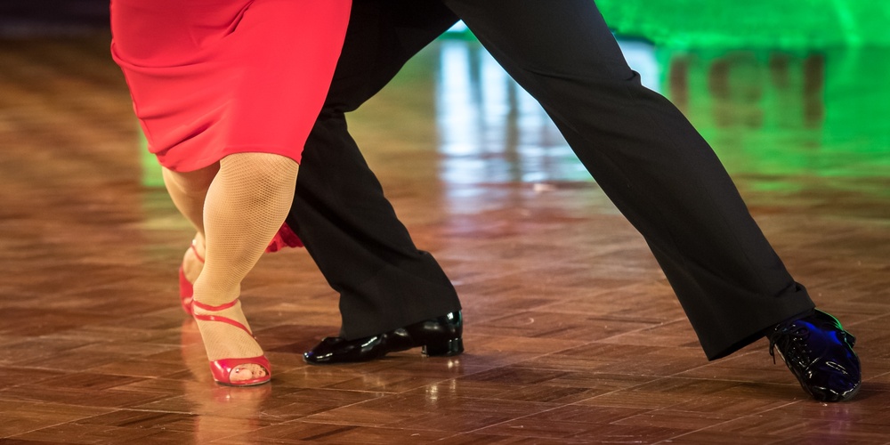 Två personer dansar tillsammans på ett dansgolv, endast deras ben och fötter syns.