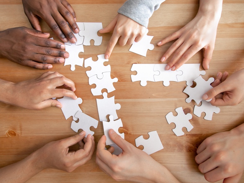 Flera händer samarbetar för att lägga ett pussel på ett trägolv.