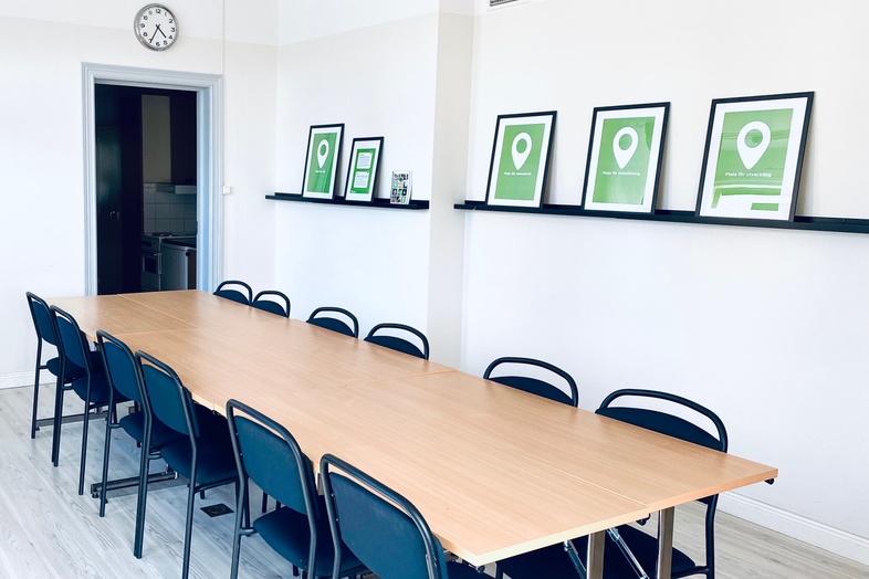 Ljust konferensrum med lång träbord, svarta stolar och gröna tavlor på väggen.