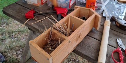 Ett träbord utomhus med verktyg, lim, träaskar och material för pyssel eller byggprojekt.