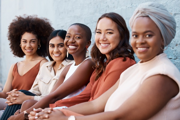 Fem kvinnor sitter i rad utomhus, ler mot kameran och ser avslappnade ut.