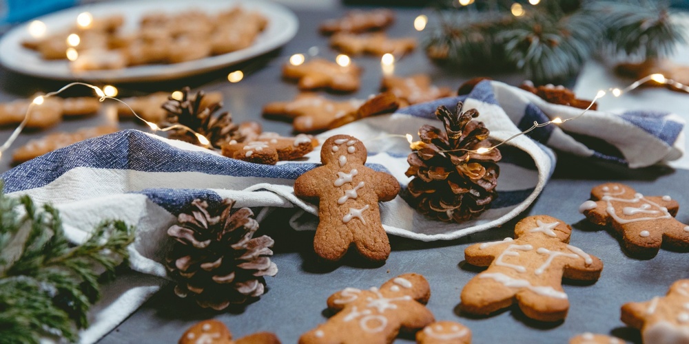 Pepparkakor dekorerade med glasyr ligger på ett bord med kottar, granris, tygservett och julbelysning.