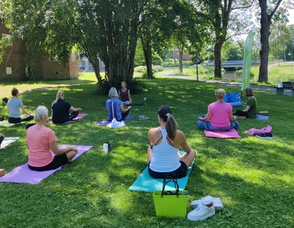 En grupp människor sitter på yogamattor utomhus i en park och deltar i en yogaklass.