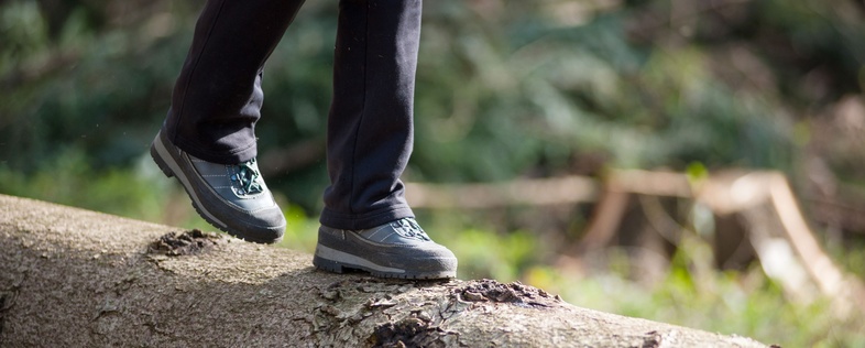 En person går på en liggande trädstam i en skog, endast benen och skorna syns.