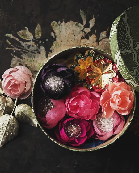 En rund ask fylld med färgglada konstgjorda blommor och dekorativa fjärilar på ett mörkt underlag.