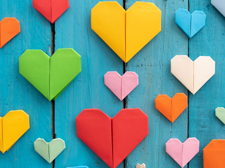 Flera färgglada origamihjärtan i olika storlekar på en blå träbakgrund.