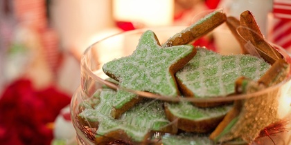 En skål med gröna stjärnformade kakor dekorerade med socker, omgiven av juldekorationer.
