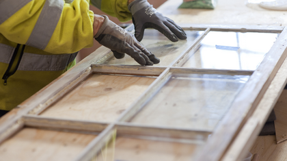 En person med handskar arbetar med att renovera ett gammalt fönster på en träbänk.