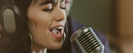 Kvinna med hörlurar sjunger i mikrofon i en studio.