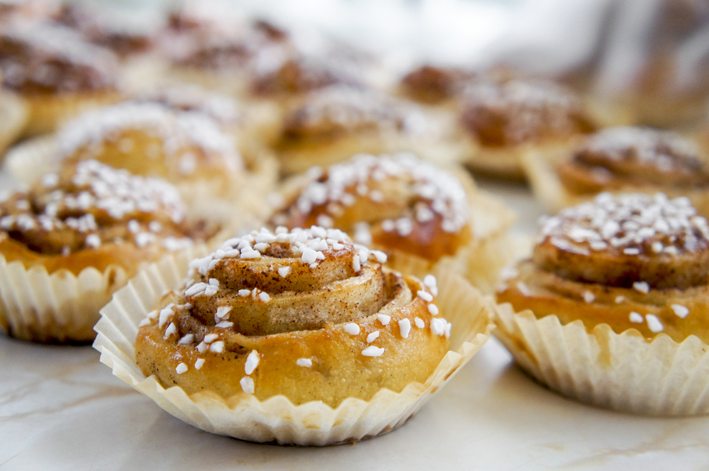 Närbild på nybakade kanelbullar med pärlsocker på toppen, placerade i vita pappersformar.