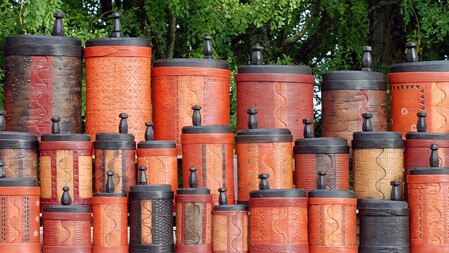 Flera färgglada, mönstrade trälådor med lock staplade utomhus framför gröna träd.