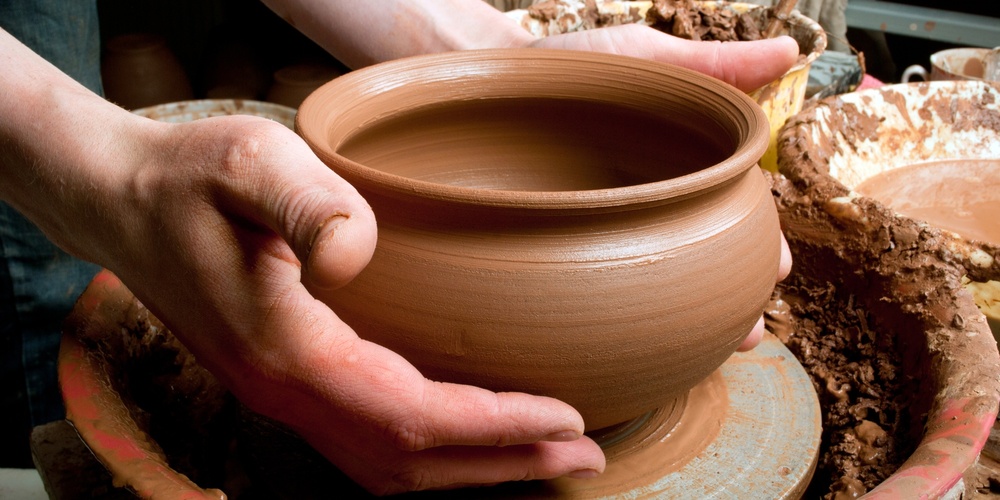 Två händer formar en lerkruka på en drejskiva i en keramikverkstad.