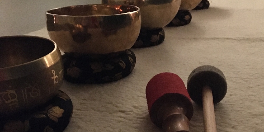 Fem tibetanska klangskålar står på rad på en matta med två klubbor framför dem i ett dämpat rum.