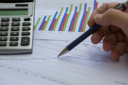 En hand håller en penna över ett papper med diagram och en miniräknare bredvid.