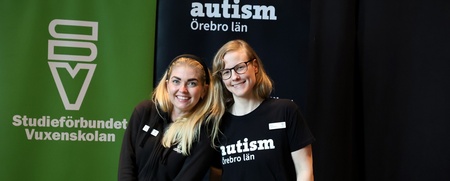 Två personer står vid ett informationsbord med broschyrer om autism och vuxenutbildning.