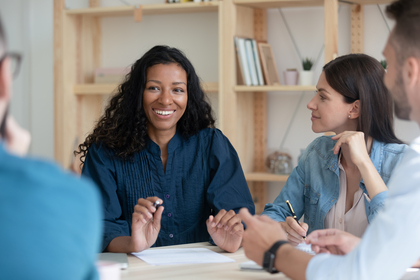 Fyra personer sitter runt ett bord och har ett möte, en kvinna i fokus ler och pratar.