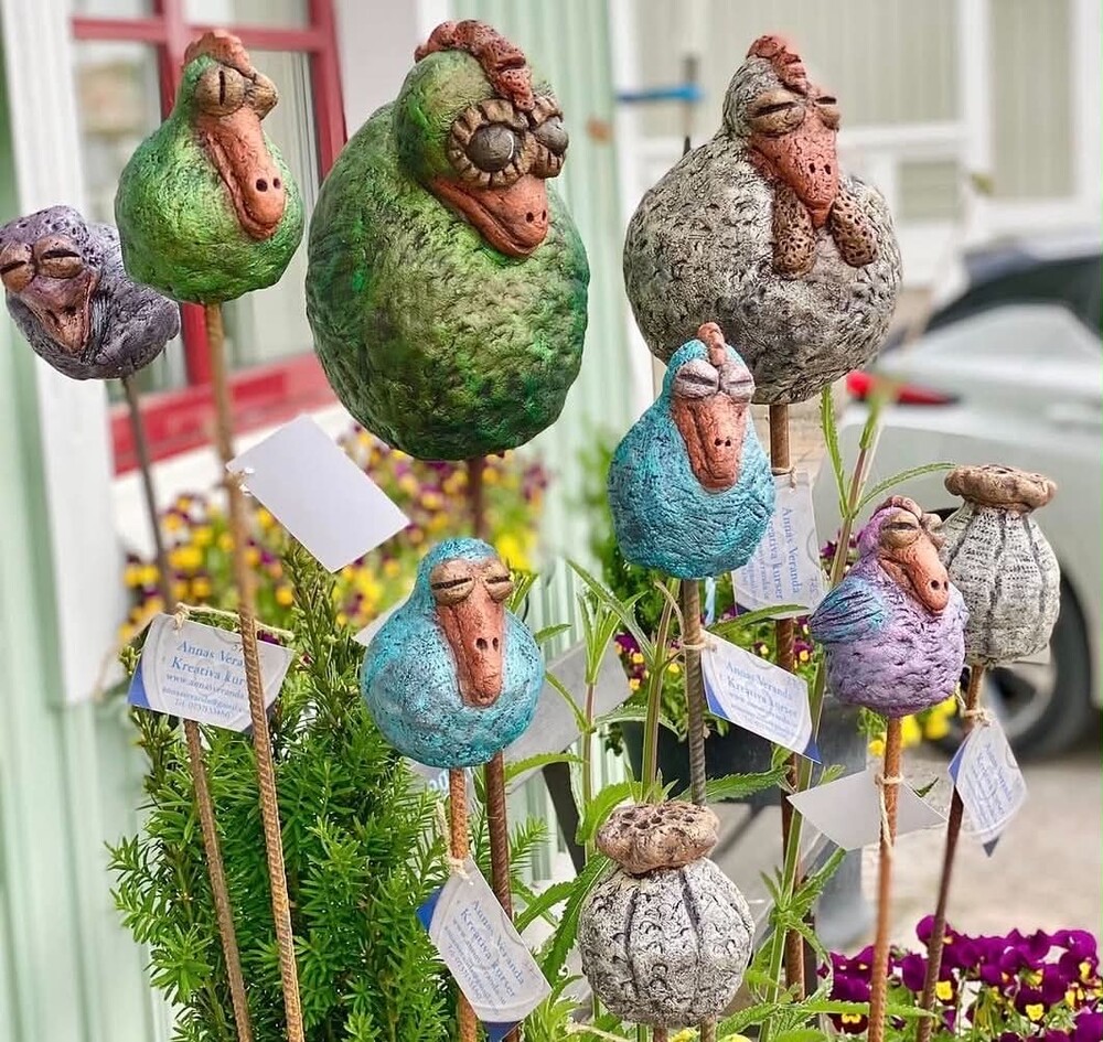 Färgglada, fantasifulla fågelliknande skulpturer på pinnar i en trädgårdsmiljö.