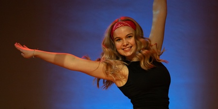 En person hoppar med utsträckta armar, klädd i svart linne och röda shorts mot en blå bakgrund.