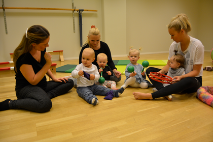 Tre vuxna och fyra små barn sitter på golvet i ett ljust rum och leker med musikinstrument.