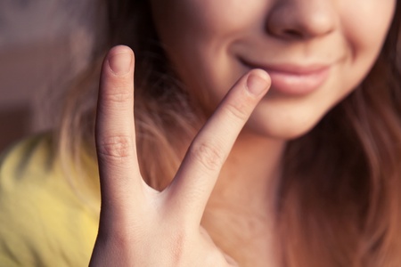 En person i gul tröja visar ett V-tecken med handen och har färgglada armband på handleden.