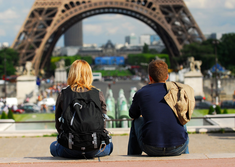 Två personer sitter med ryggen mot kameran och tittar mot Eiffeltornet i Paris.