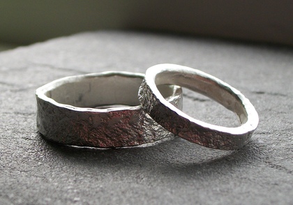 Två silverringar med grov yta ligger på en mörk yta.