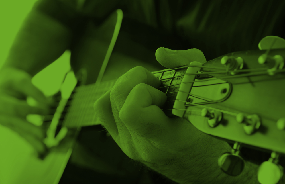 Närbild på en person som spelar akustisk gitarr, bilden har ett grönt färgfilter.