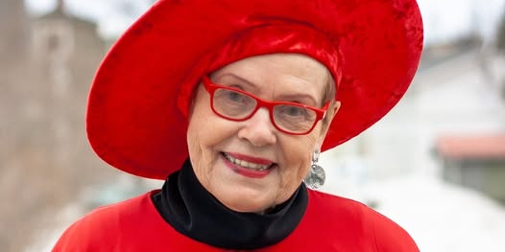 Person klädd i röd mantel och stor röd hatt står utomhus på vintern.