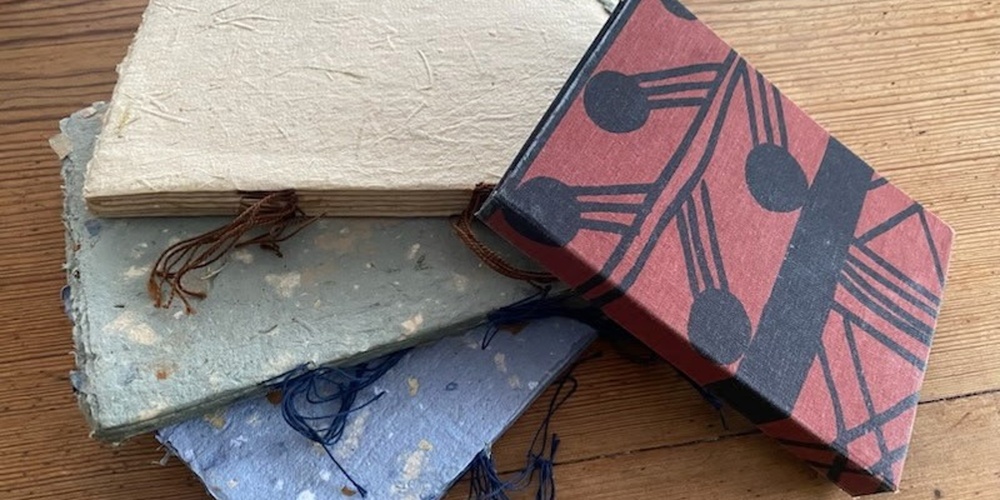 Fyra handgjorda anteckningsböcker med färgglada omslag ligger på ett träbord.