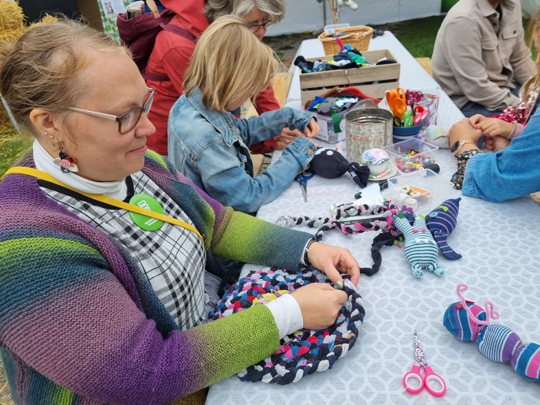 Flera personer sitter vid ett bord utomhus och pysslar med tyg och garn.