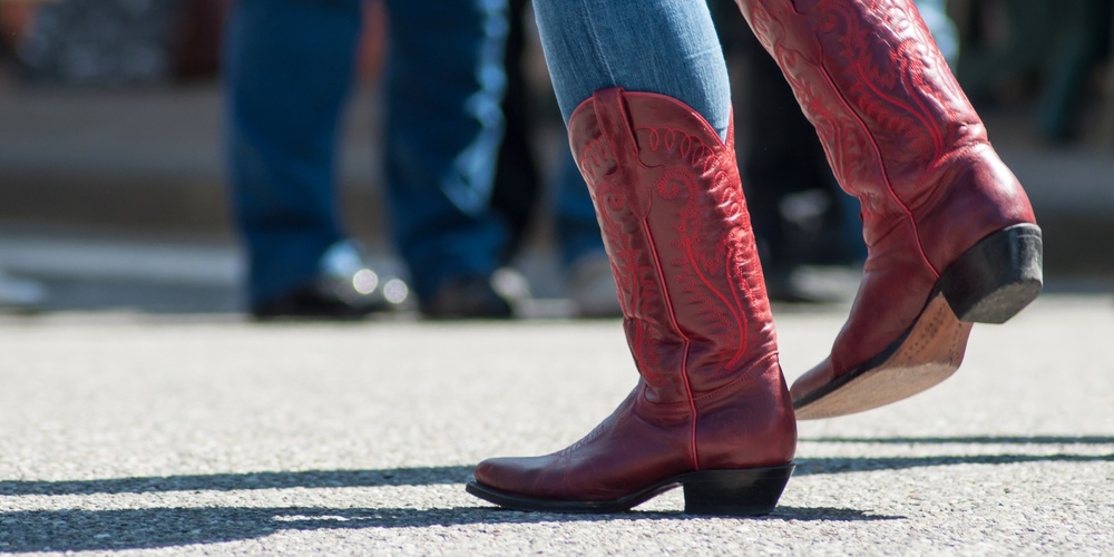 Person i blå jeans och röda cowboyboots dansar utomhus på asfalt.