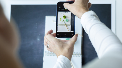 En person fotograferar ett anteckningsblock med penslar och färgkoppar med en smartphone.
