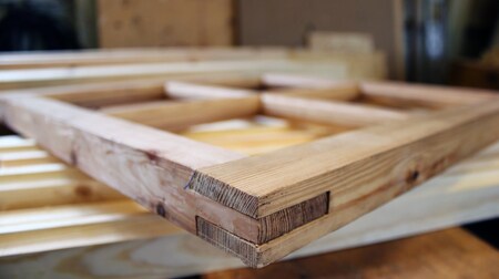 Närbild på en träram med synliga hörnsnickerier, liggande på ett arbetsbord i en verkstad.