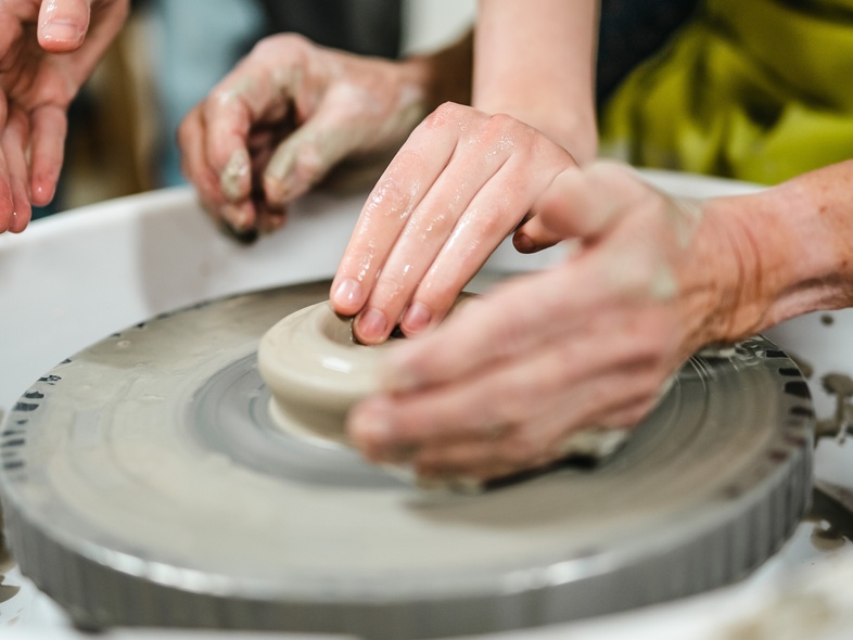 Två personer formar lera på en drejskiva med sina händer i en keramikverkstad.